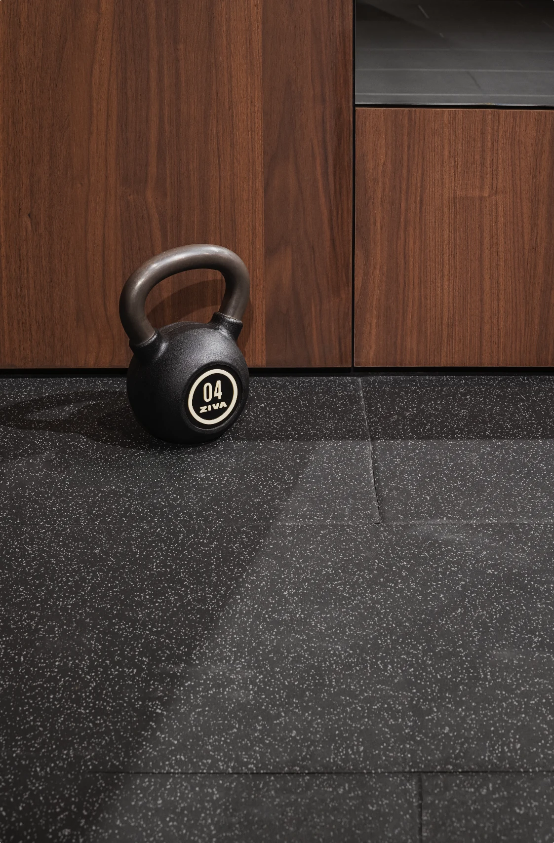 A kettlebell on the rubber floor beside walnut cabinetry