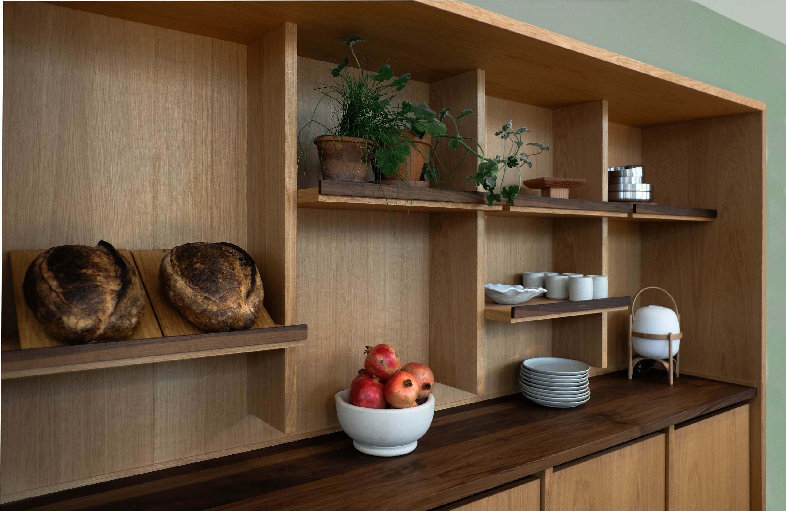 Oak and walnut display shelving in the Charlottehaven lobby, styled with bread, plants and ceramics