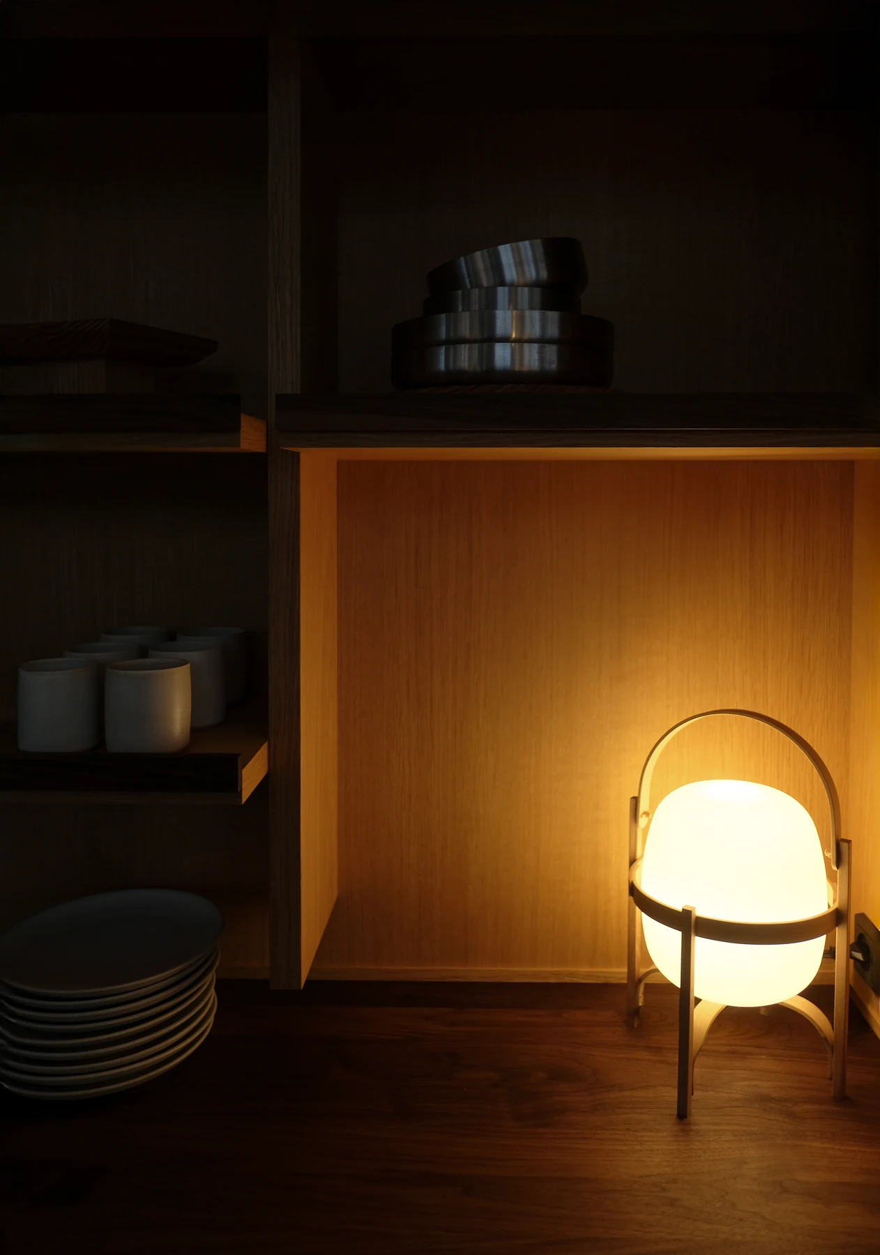 Portable lamp glowing in a darkened oak niche beside stacked plates