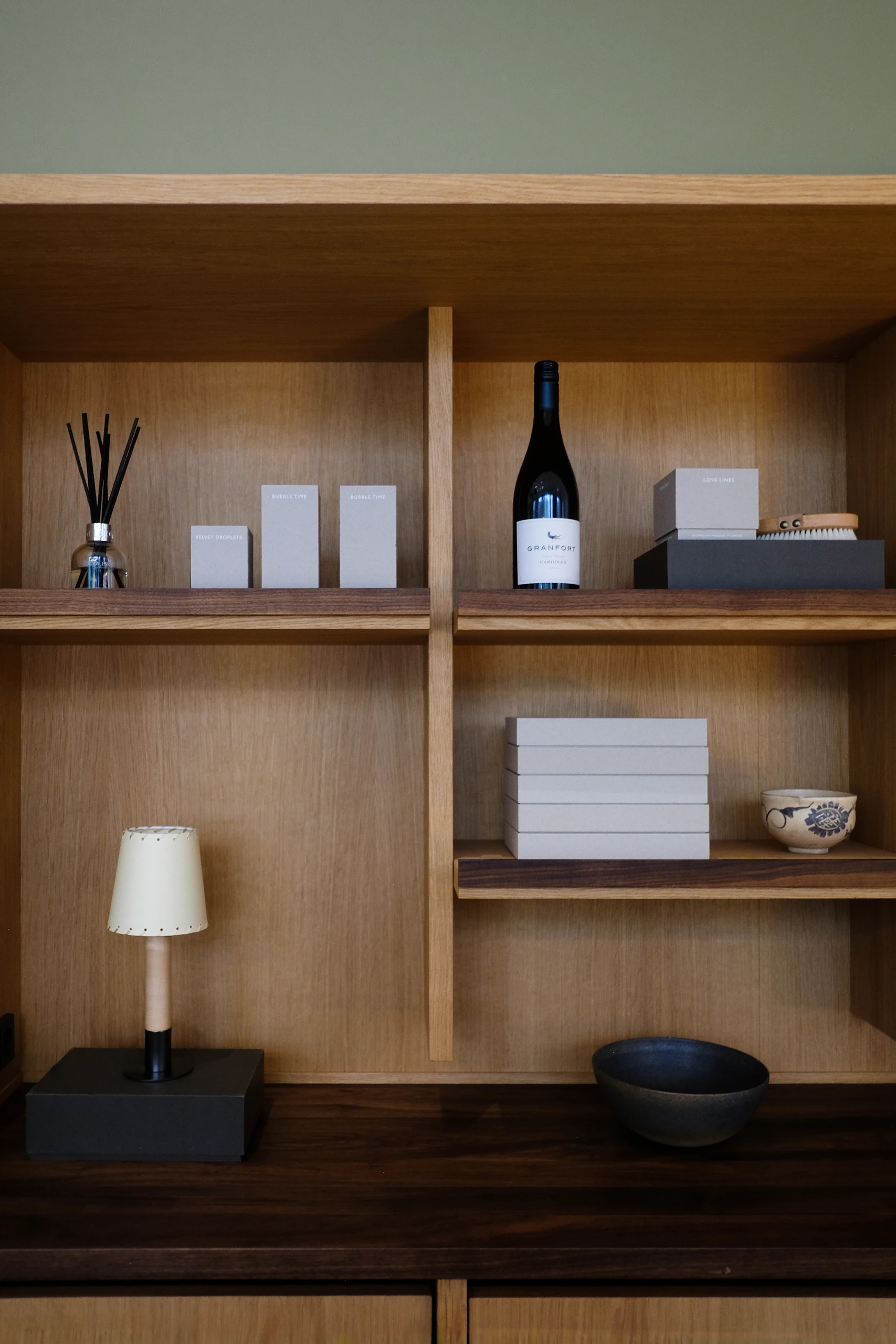 Oak shelving displaying ceramics and books against a soft green wall