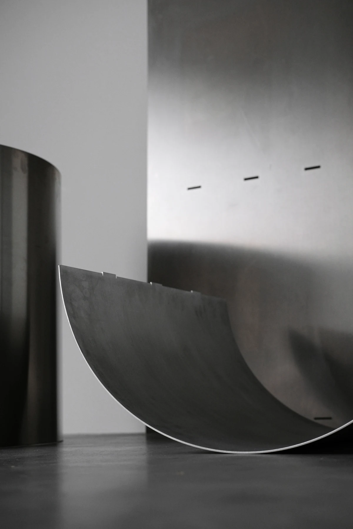 The rolled aluminium curve catching a gradient of light against a dark ground