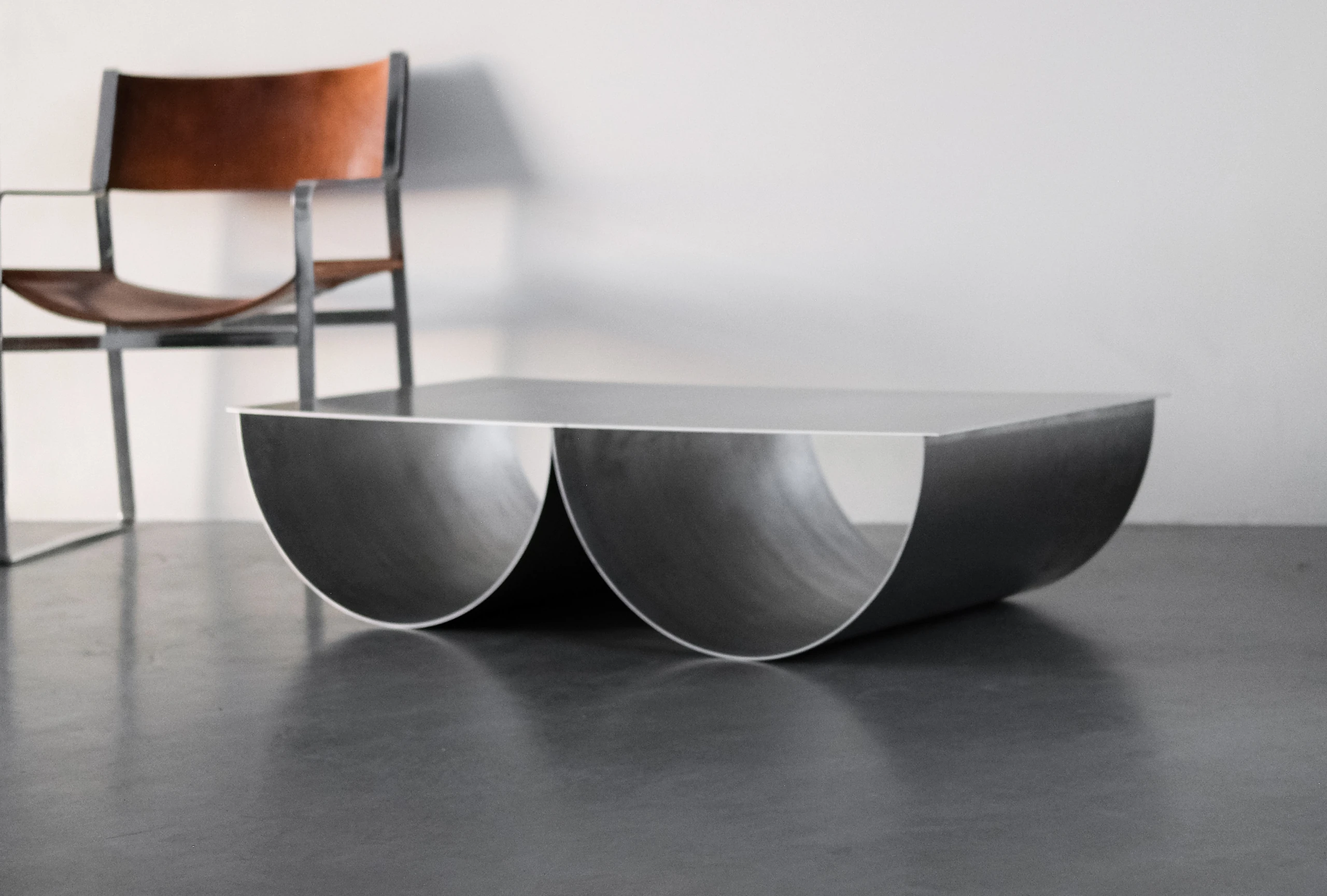 The IB table in brushed aluminium, its two rolled curves meeting beneath a sharp tabletop
