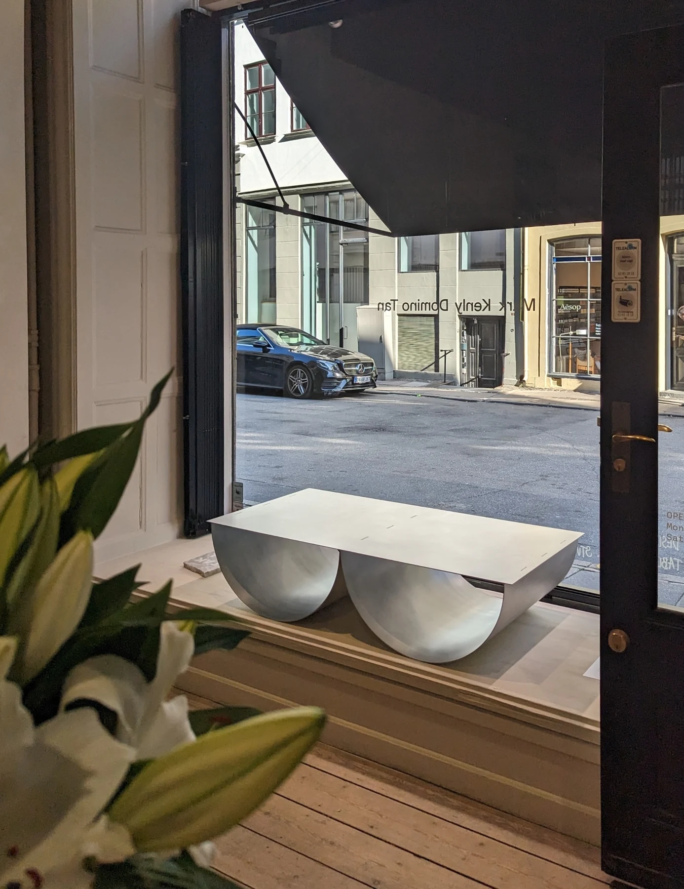 The table in the shop window seen from inside, past lilies in the foreground