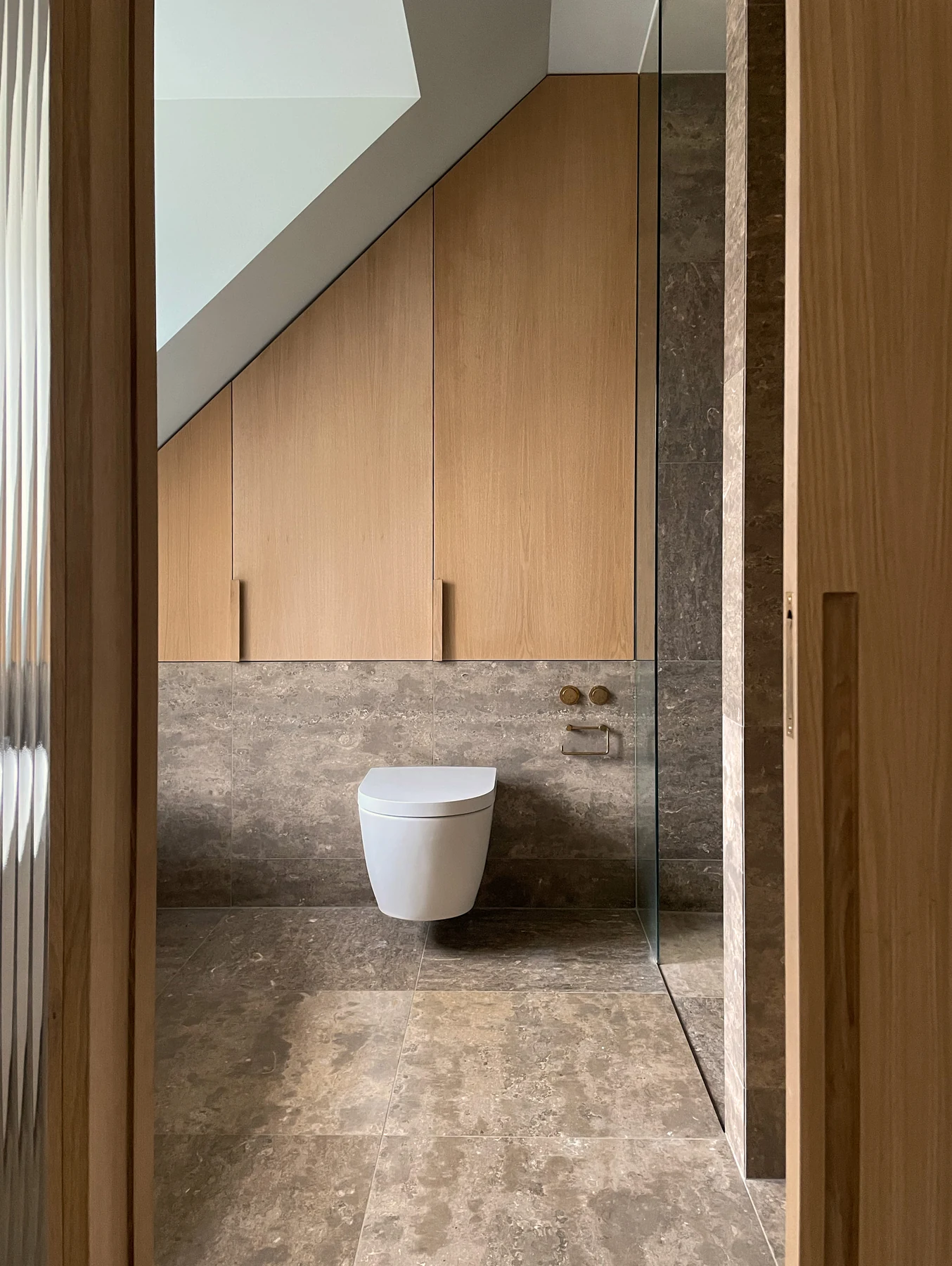 Bathroom under a sloped ceiling with stone tiling and oak joinery