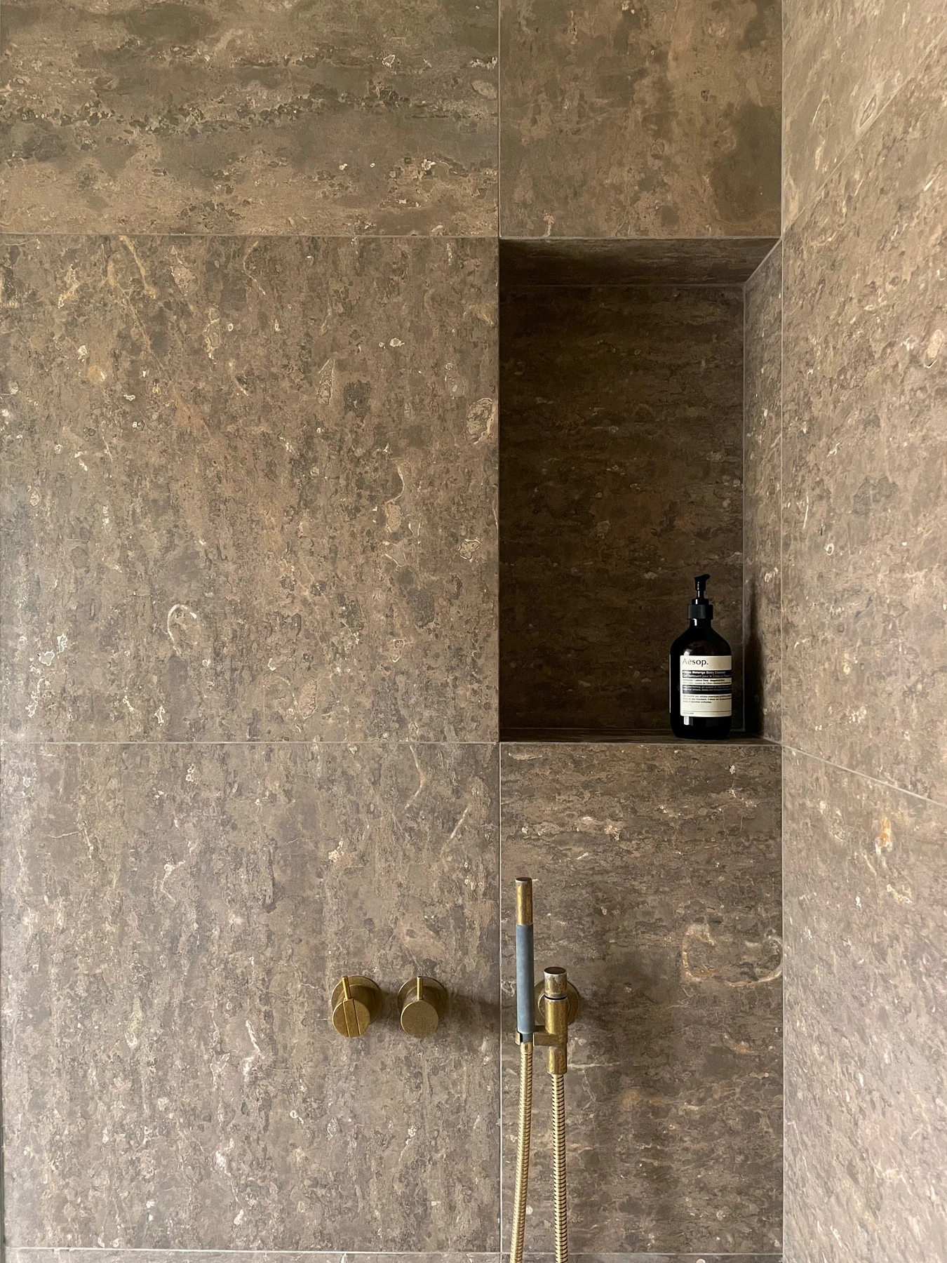 Shower in veined stone with brass fittings and a recessed niche