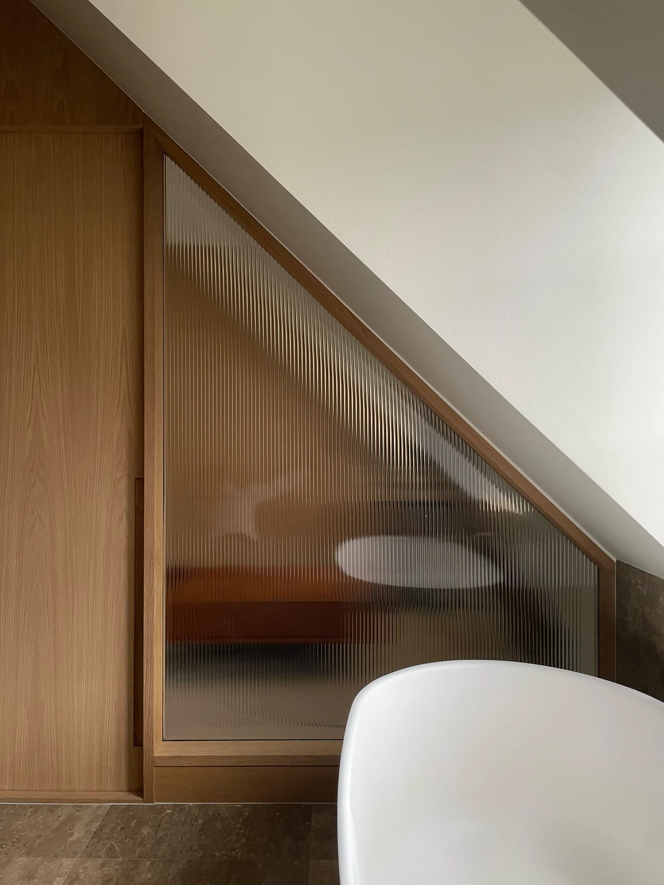 Freestanding bath behind a reeded glass screen beneath the roof slope